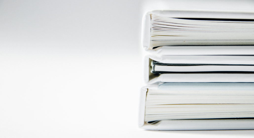 Close-up of a stack of white bound documents or binders against a plain white background, clean and minimal mood.